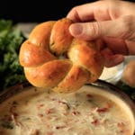 dipping garlic asiago knot into zuppa toscana