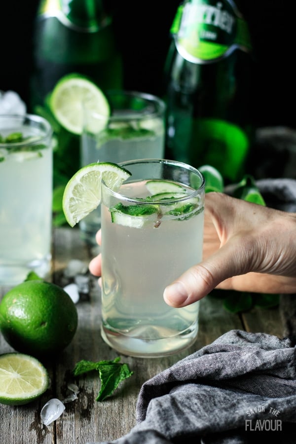 person holding a glass of lime and mint refresher with a lime slice on the rim of the glass