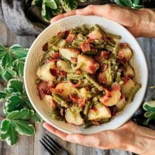 person holding a bowl of Southern green beans and potatoes
