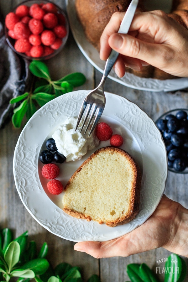 person holding a white plate of sour cream pound cake with fork