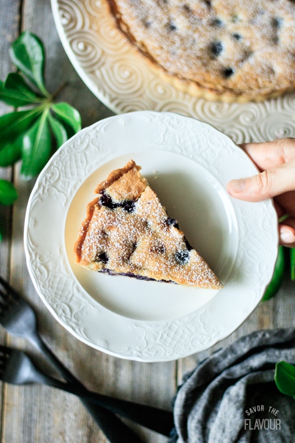 holding a slice of blueberry frangipane tart on a plate