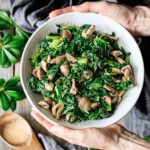 holding a bowl of sautéed kale with mushrooms