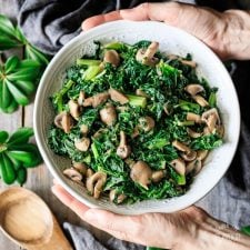 holding a bowl of sautéed kale with mushrooms