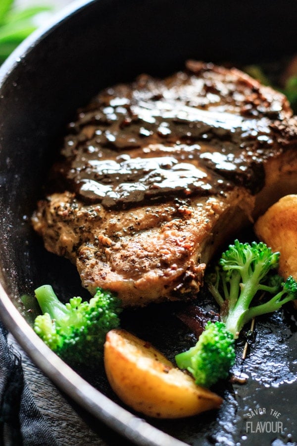 closeup of a pork chop in a cast iron skillet with veggies