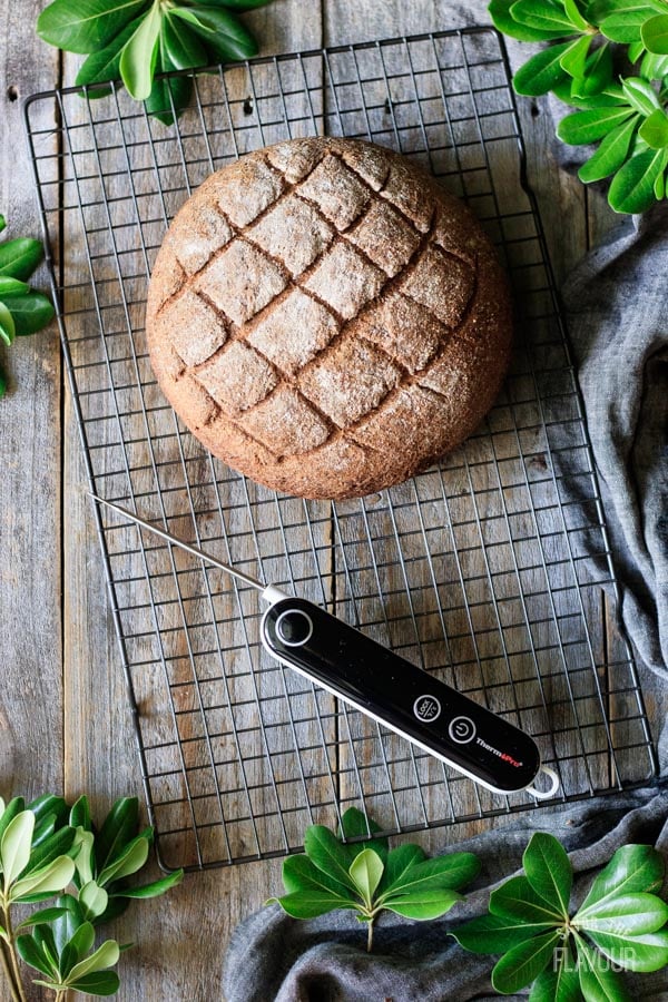 loaf of pumpernickel bread with a thermometer on a cooling rack