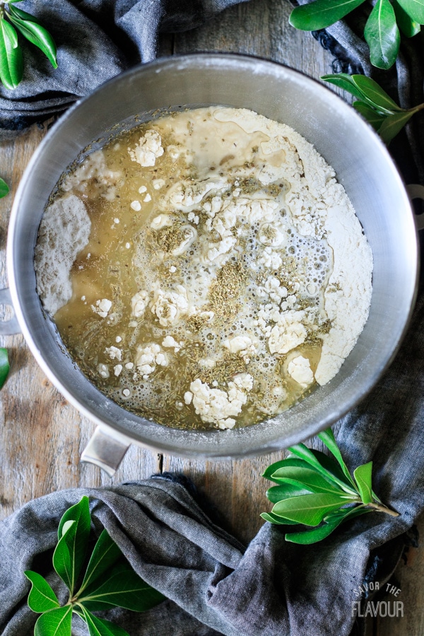 adding sugar, oil, rosemary, and water to flour mixture