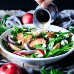 pouring dressing on a bowl of spinach apple salad