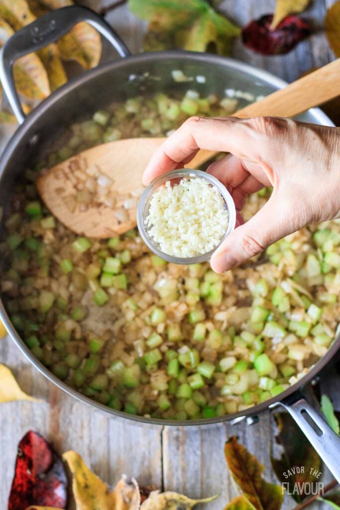 adding minced garlic to cooked veggies