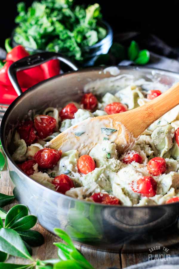person stirring tortellini with alfredo basil sauce