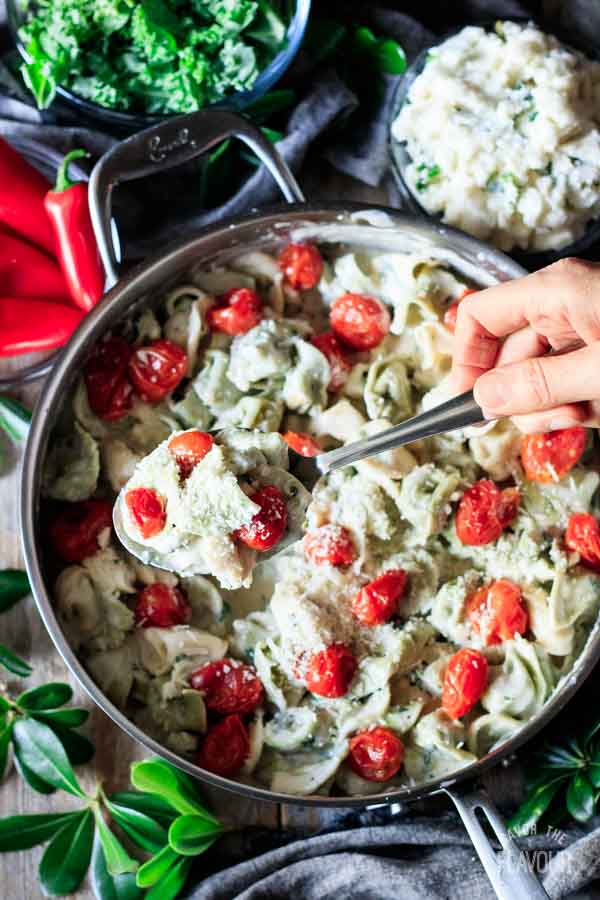 person holding a spoonful of tortellini in alfredo basil sauce
