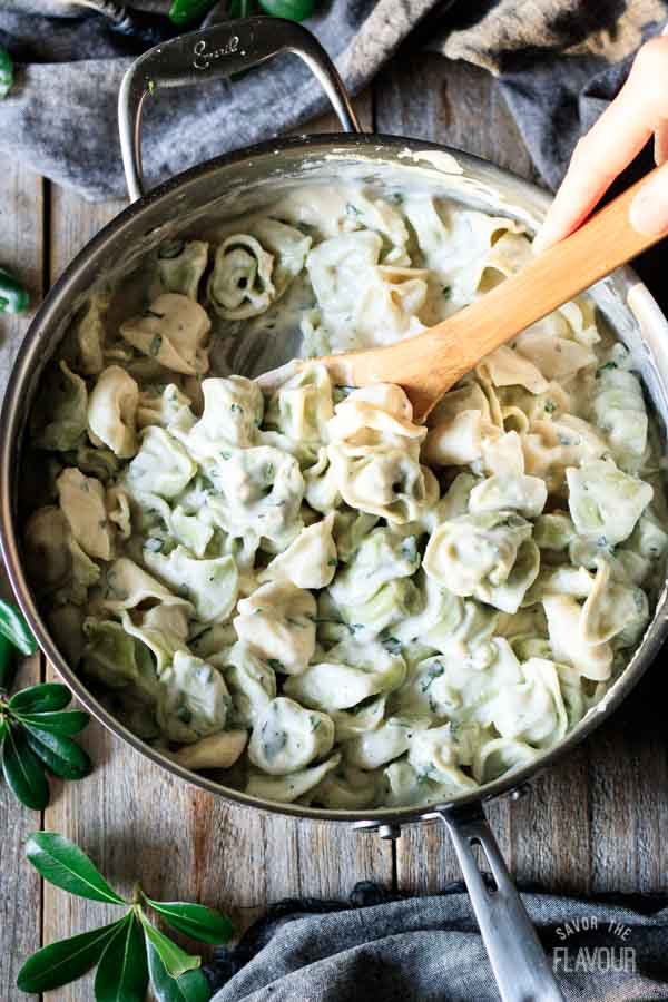 person stirring tortellini into alfredo basil sauce