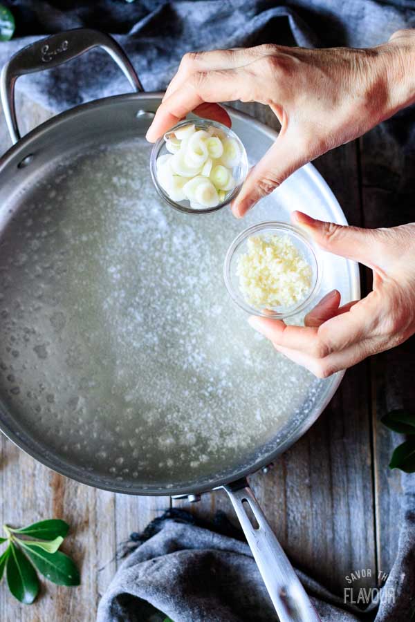 person holding bowls of green onion and garlic
