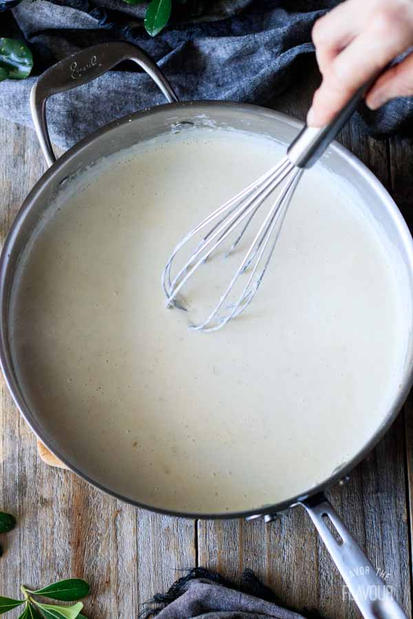 person whisking alfredo sauce in a pan