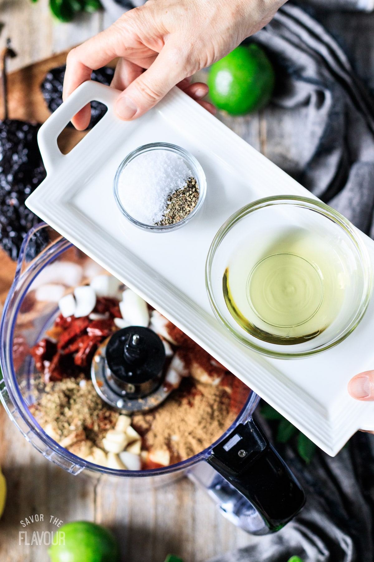 person adding salt, pepper, and olive oil to a food processor