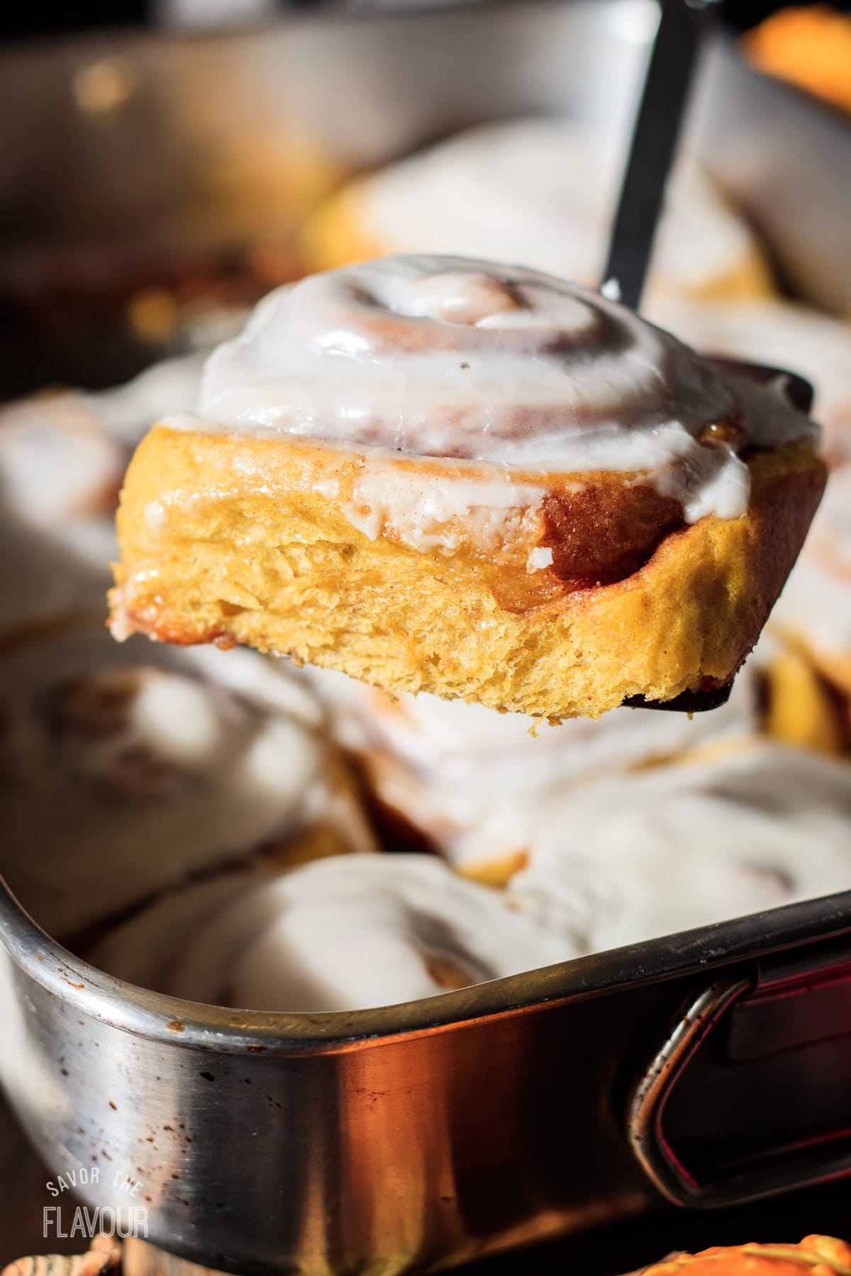 a pumpkin cinnamon roll being lifted from the pan with a spatula