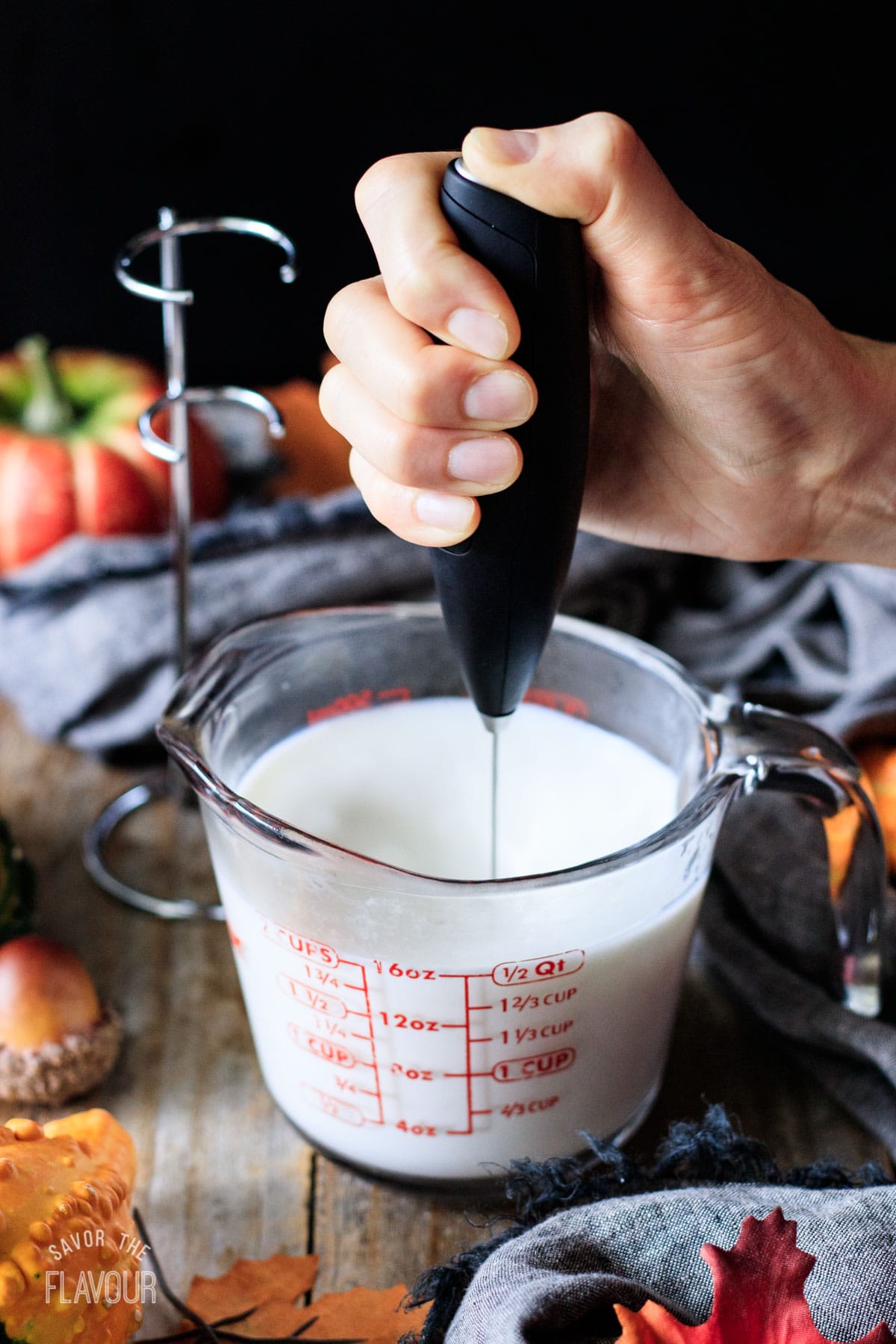 person frothing steamed milk in a glass measuring cup