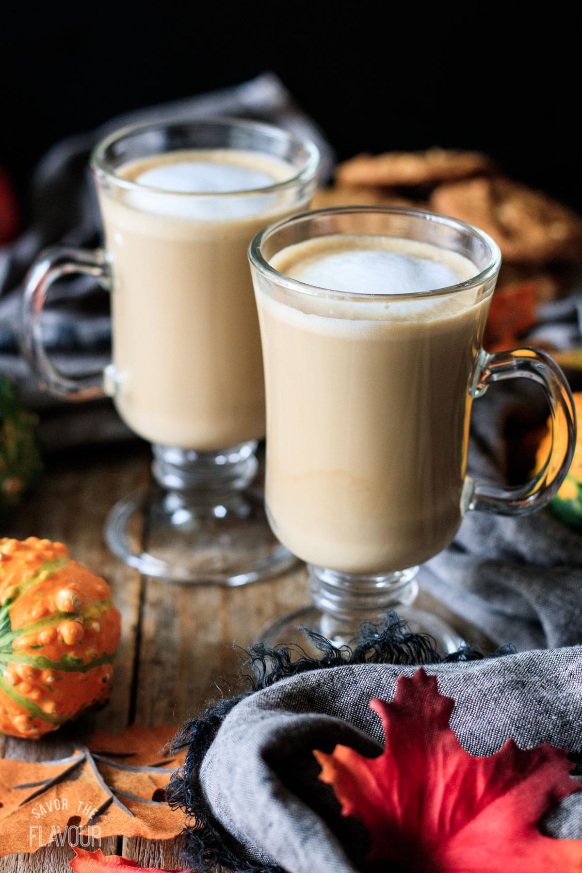 two glass mugs of flat white with fall leaves and gourds