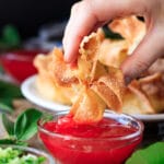 person dipping a deep fried cream cheese rangoon into a bowl of sauce