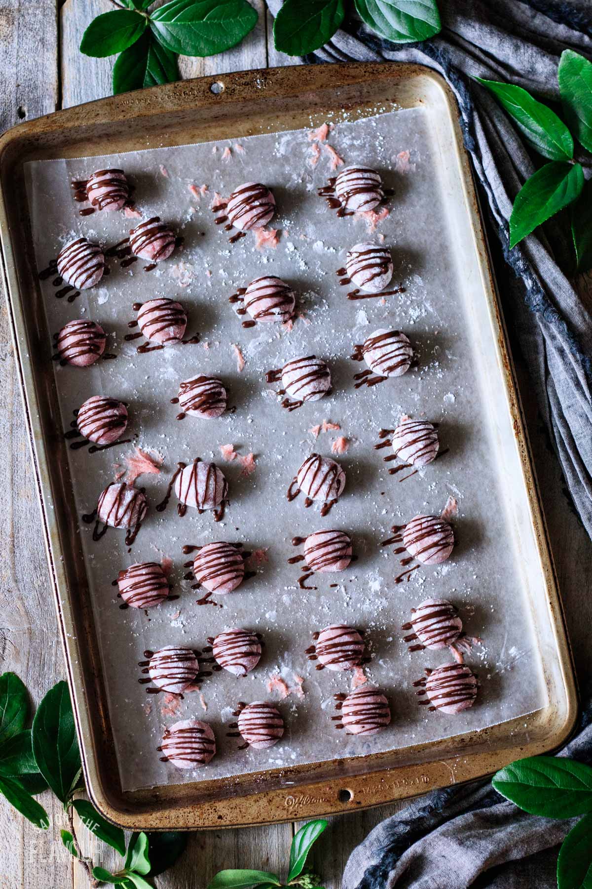 strawberry truffles drizzled with chocolate on a cookie sheet