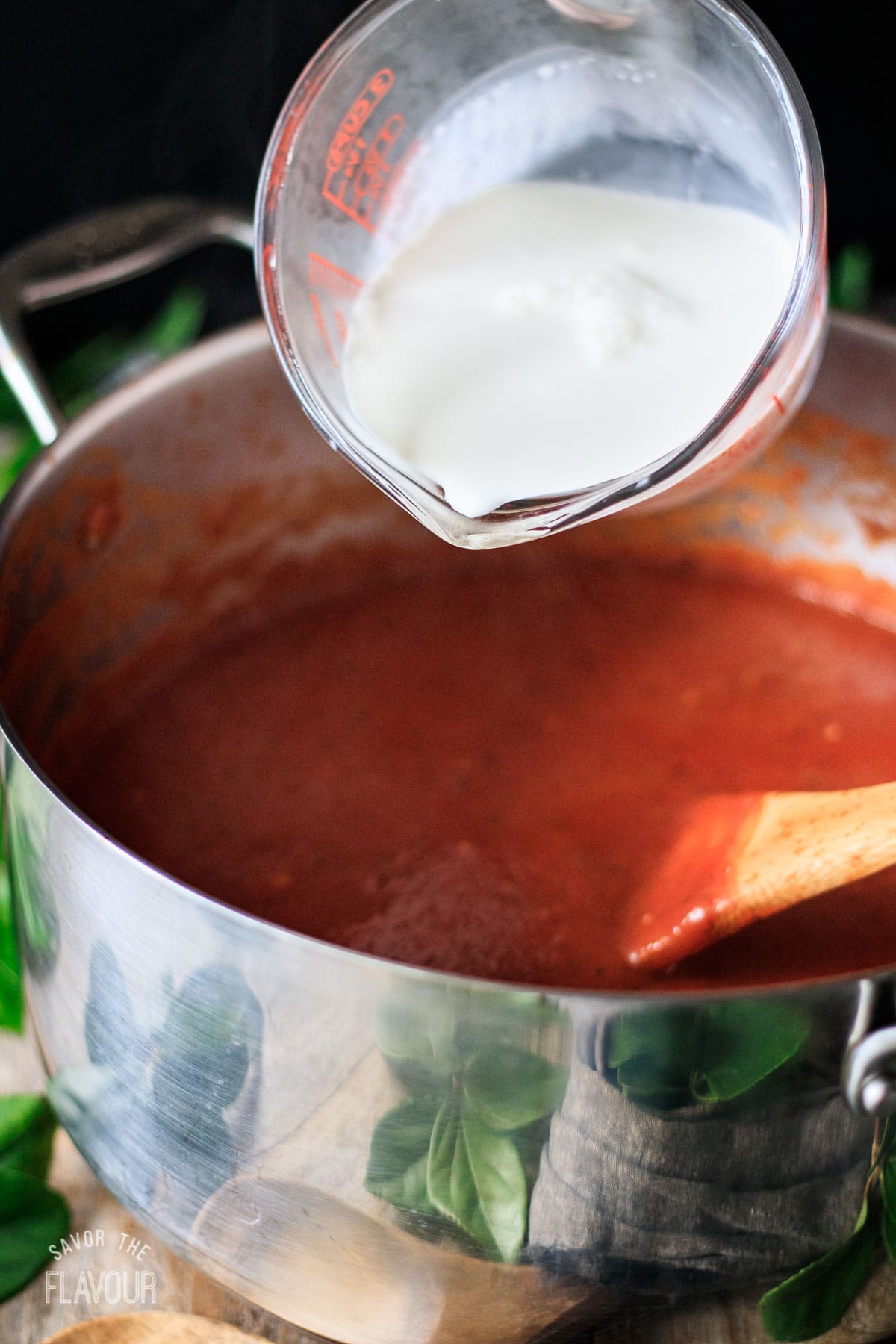 person adding cream to the pot of tomato soup