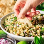 person dipping a tortilla chip into corn salsa