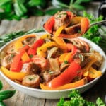 person holding a spoonful of sausage, peppers, and onions