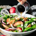 pouring the dressing over the spinach apple salad