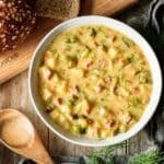 bowl of dill pickle soup with bread and a wooden spoon