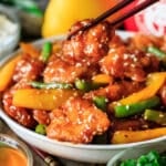 holding a piece of honey sesame chicken with chopsticks