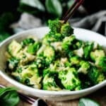 person holding a piece of broccoli with chopsticks
