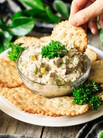 person dipping a cracker into sardine salad