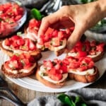 person holding a piece of caprese bruschetta