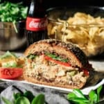 serving a slice of the Sicilian tuna sandwich with tomato and chips