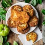 white serving plate of fried green tomatoes with one on a piece of parchment paper.