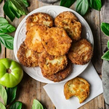 white serving plate of fried green tomatoes with one on a piece of parchment paper.