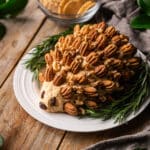 hedgehog cheese ball on a white plate with a bowl of crackers.