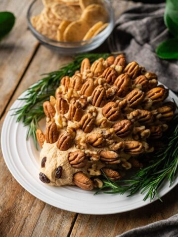 hedgehog cheese ball on a white plate with a bowl of crackers.