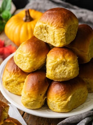 plate of pumpkin dinner rolls in a stack.