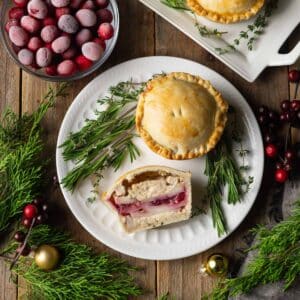 half of a turkey cranberry mini pie on a plate with herbs.
