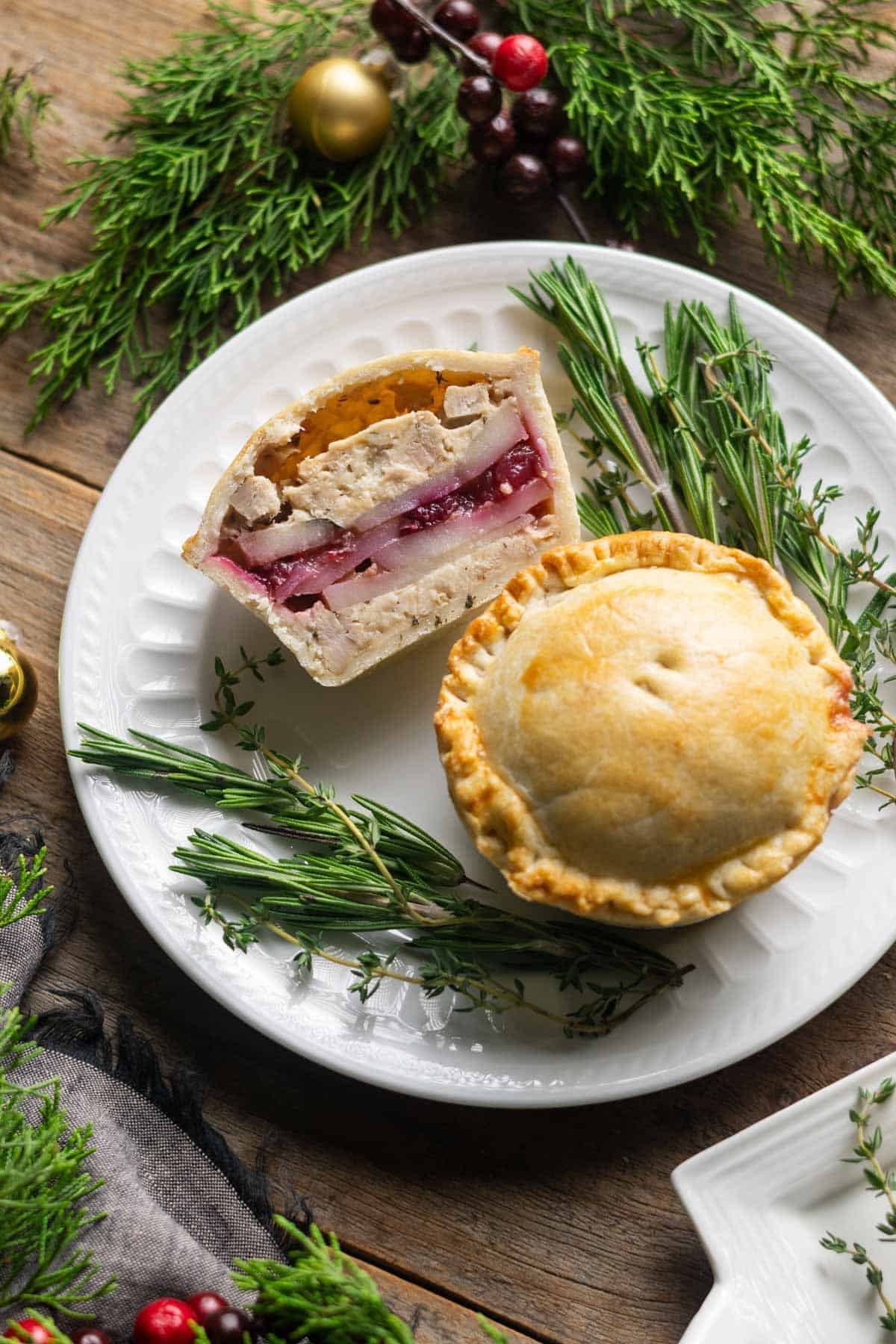 turkey cranberry mini pie cut in half on a plate with herbs.
