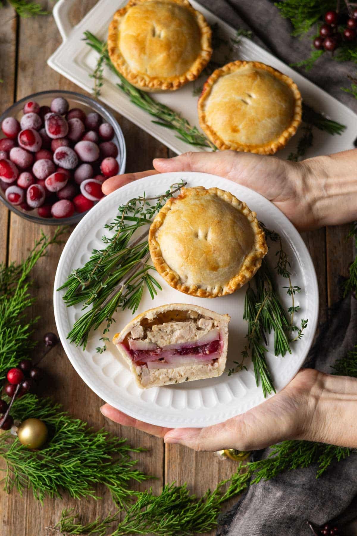 holding a plate of turkey cranberry mini pies with fresh herbs.