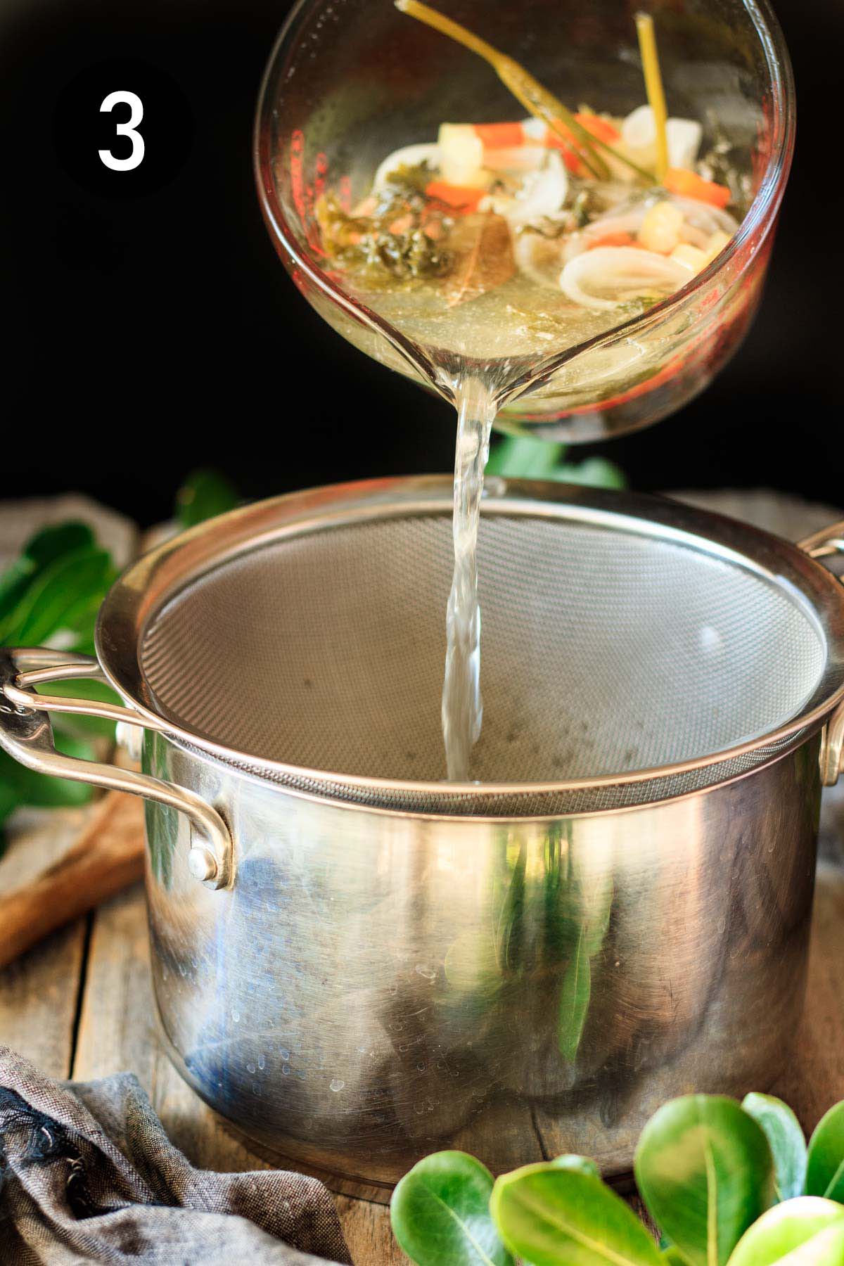 pouring chicken broth through a strainer and into a pot.