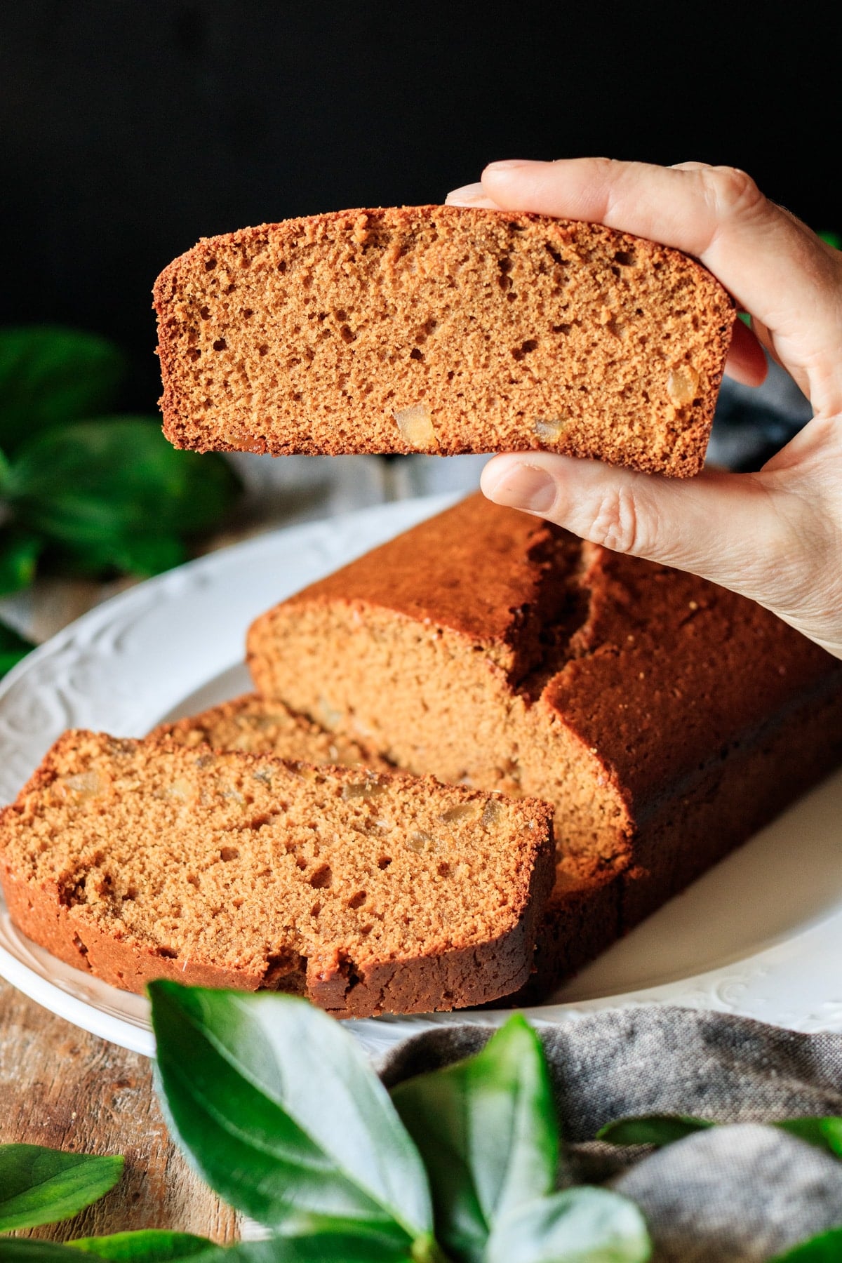 person holding a slice of Jamaican ginger cake above the platter of cake.