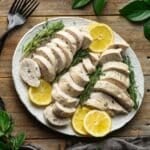 white oval platter of sliced chicken and lemons.