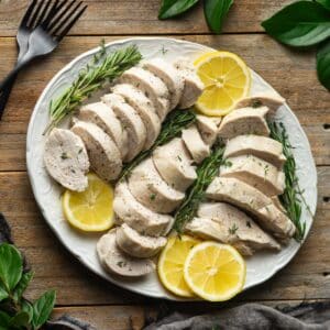 white oval platter of sliced chicken and lemons.