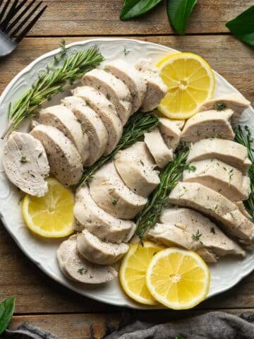 white oval platter of sliced chicken and lemons.