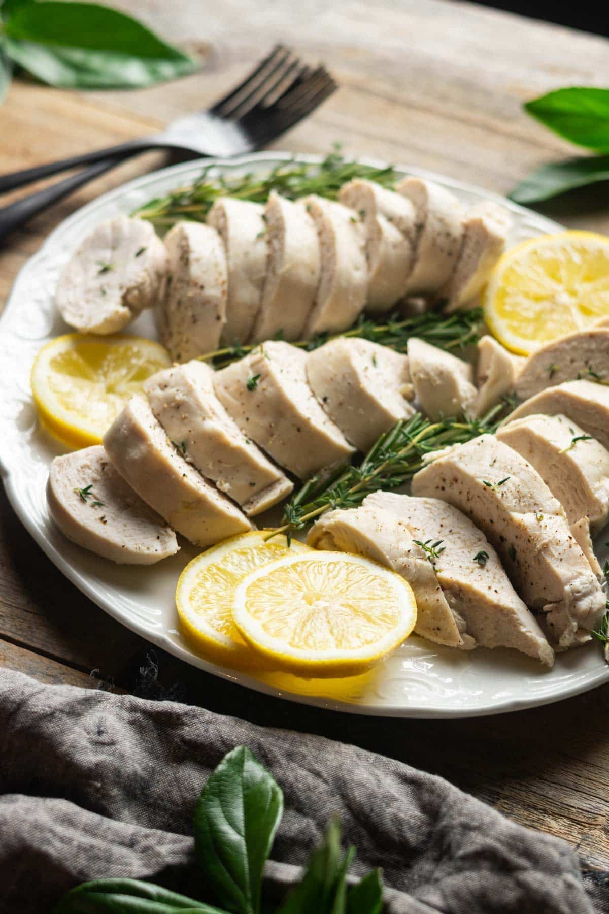 three sliced chicken breasts on a white platter with stacks of lemon slices.