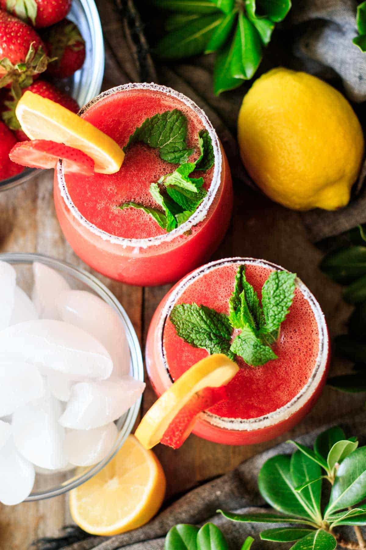 two glasses of frozen strawberry lemonade garnished with mint sprigs.