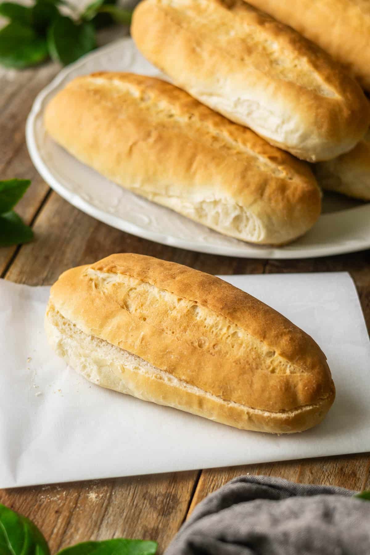 hoagie roll on a piece of parchment with a platter of rolls in the background.