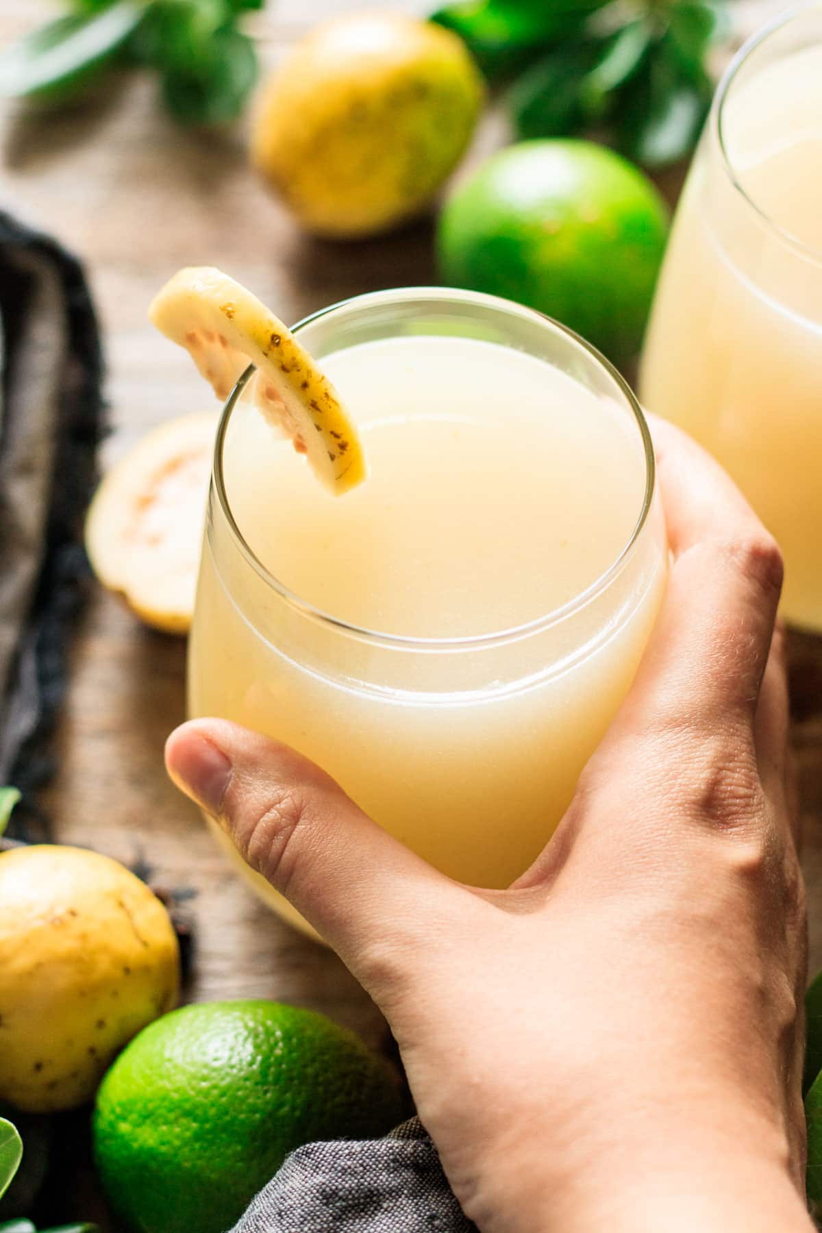 holding a glass of agua de guayaba garnished with a thin slice of guava.
